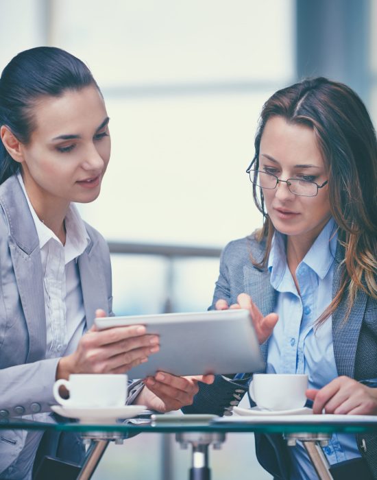 Image of two confident businesswomen working with touchpad in office